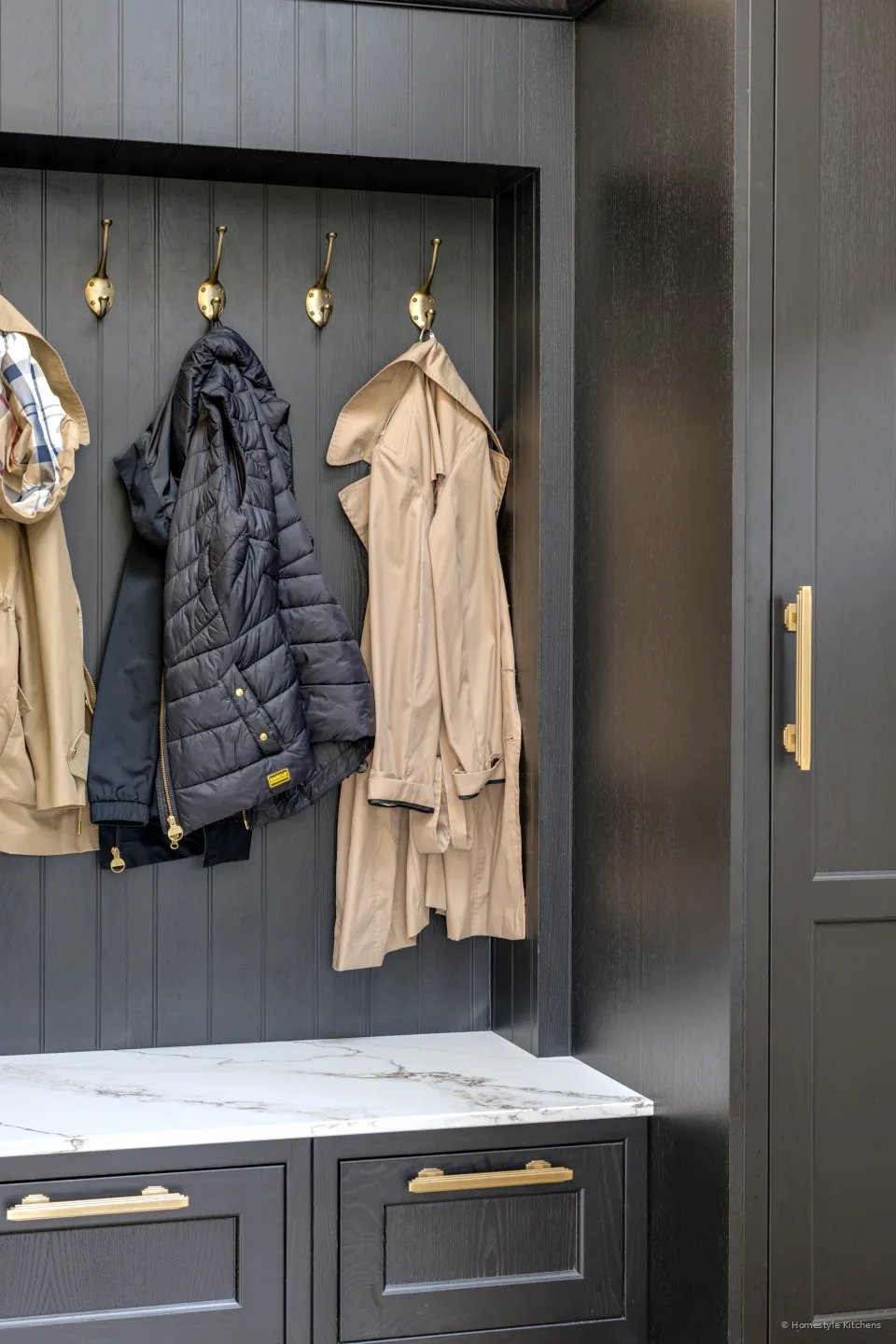 Tall charcoal coat cupboard with brass handle, white quartz bench and coats.