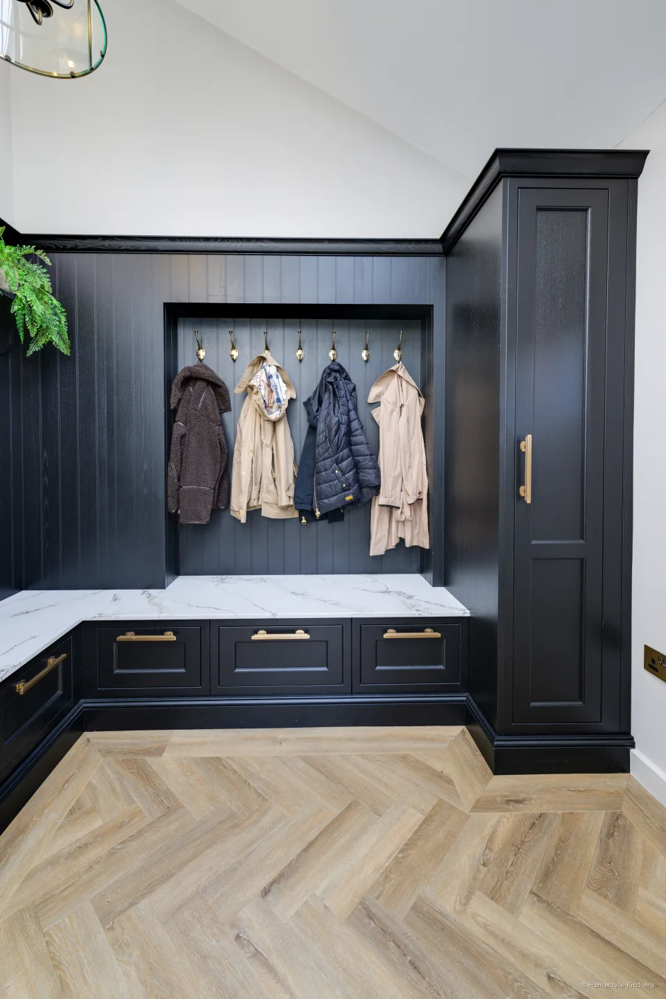 Charcoal boot room with a white quartz bench, brass hooks and coat storage.