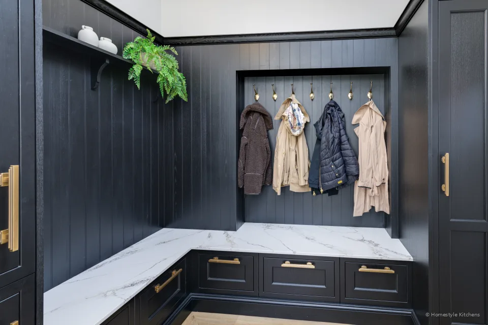 Wide boot room in charcoal cabinetry, white quartz L-bench and brass hooks.