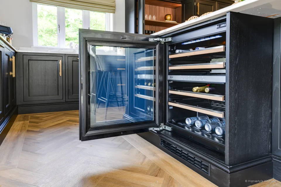 Open charcoal drinks cupboard with glassware and bottles, white quartz beside.