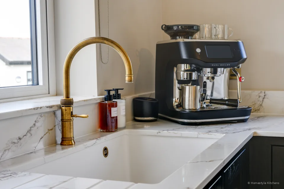 White Caple undermount and Quooker Fusion in patinated brass under a window.