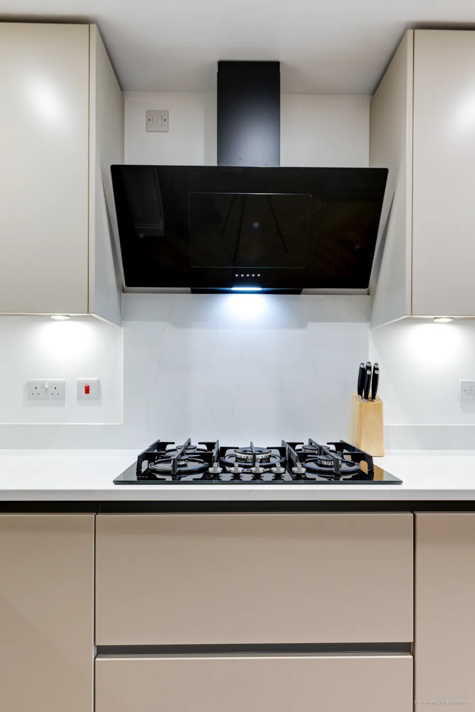 Black gas hob and angled black glass extractor against pale grey handleless units.