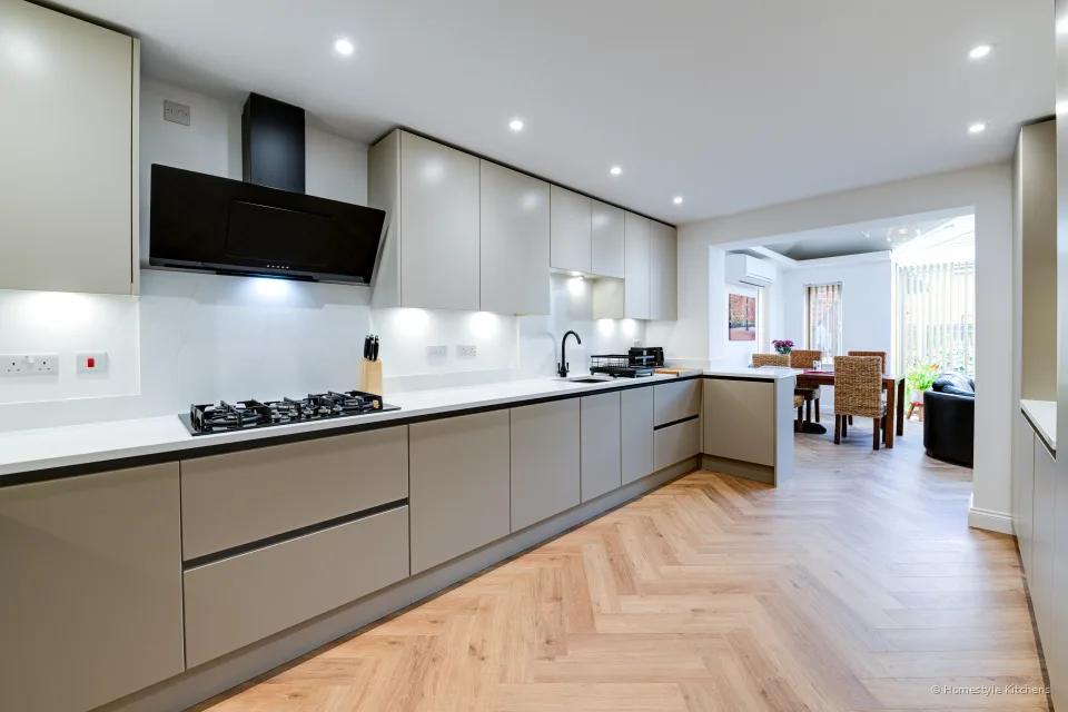 Pale grey handleless kitchen with Calacatta Gold worktops, black gas hob and angled extractor.