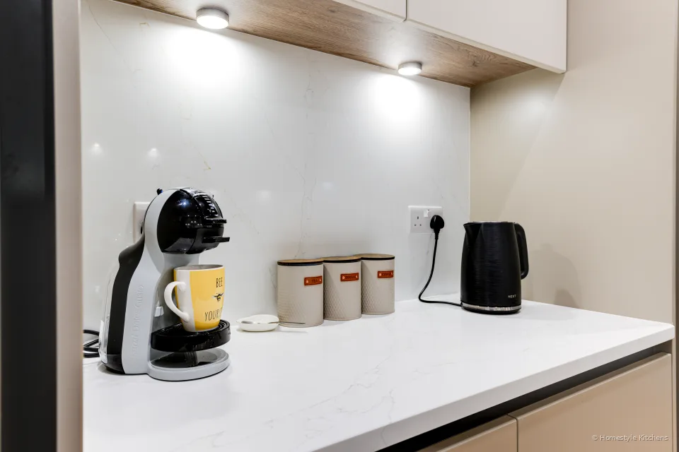 Coffee station on pale worktop with black coffee machine and pale grey cabinets.