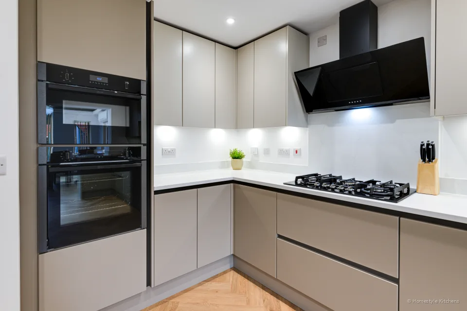 Corner of pale grey cabinets, black tall ovens and black angled extractor.