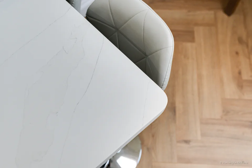 Rounded pale worktop edge against pale grey cabinetry and herringbone floor.
