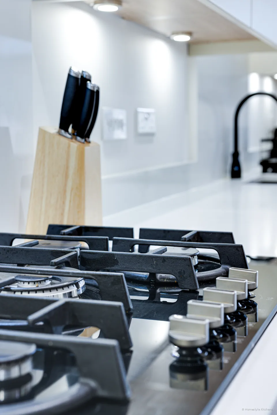 Close on the black gas hob and knife block on white quartz.