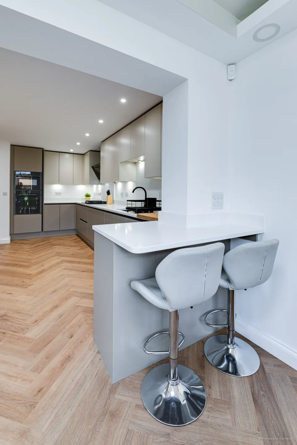 Island breakfast bar with stools, pale grey cabinetry and open dining beyond.