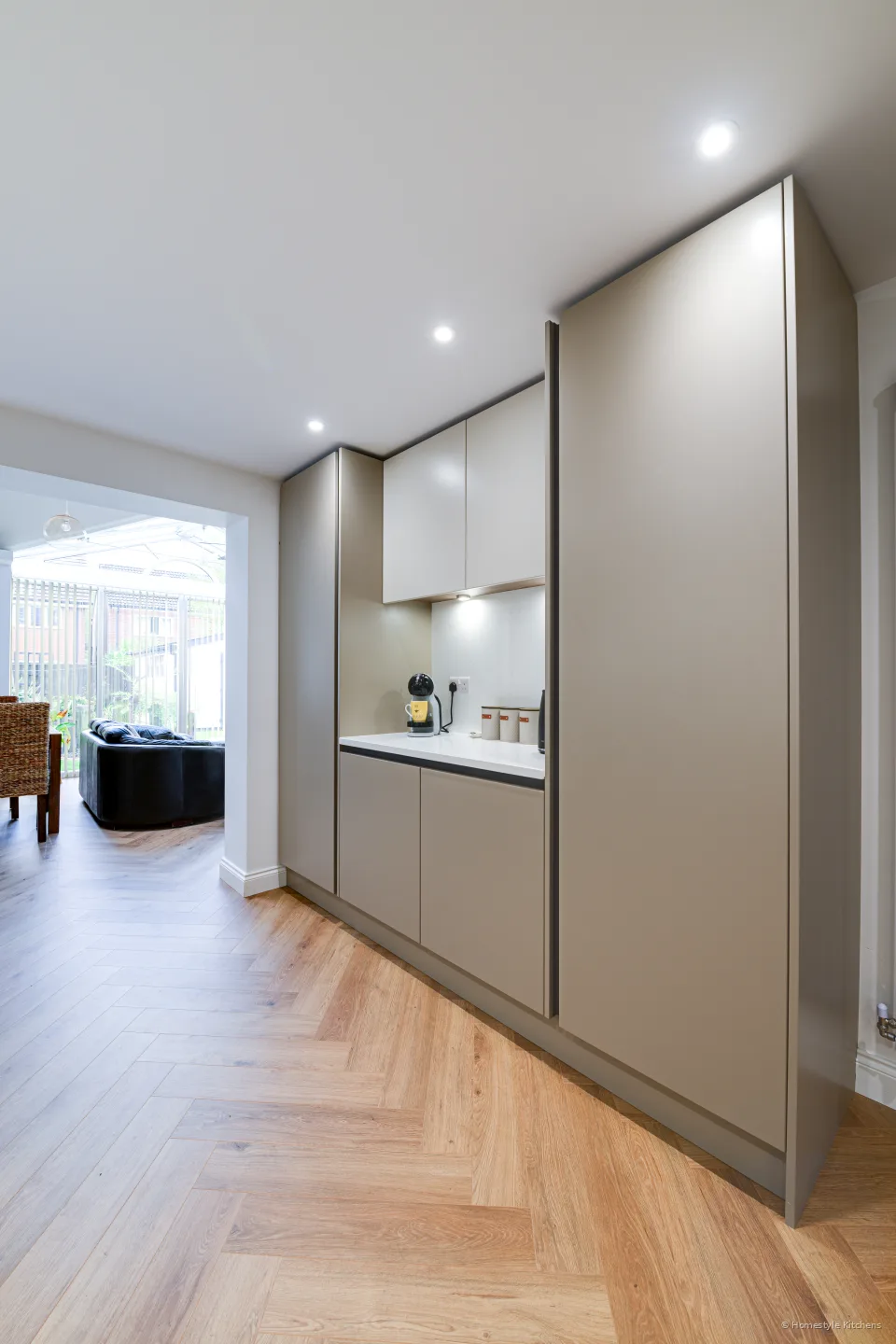 Looking down the kitchen past tall pale grey units and the worktop run.