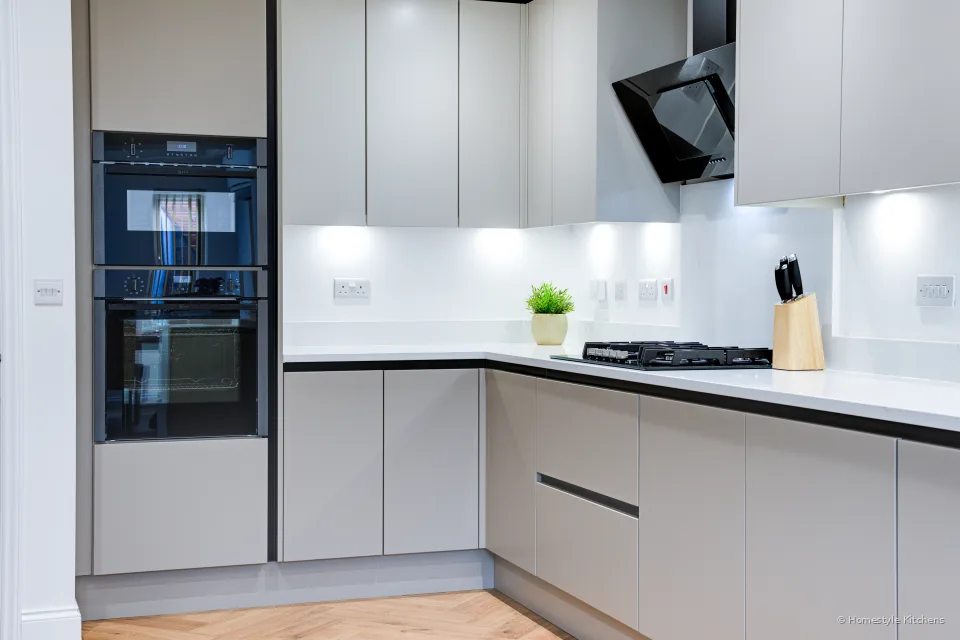 Angled run with black tall ovens, black hob and pale grey cabinets.