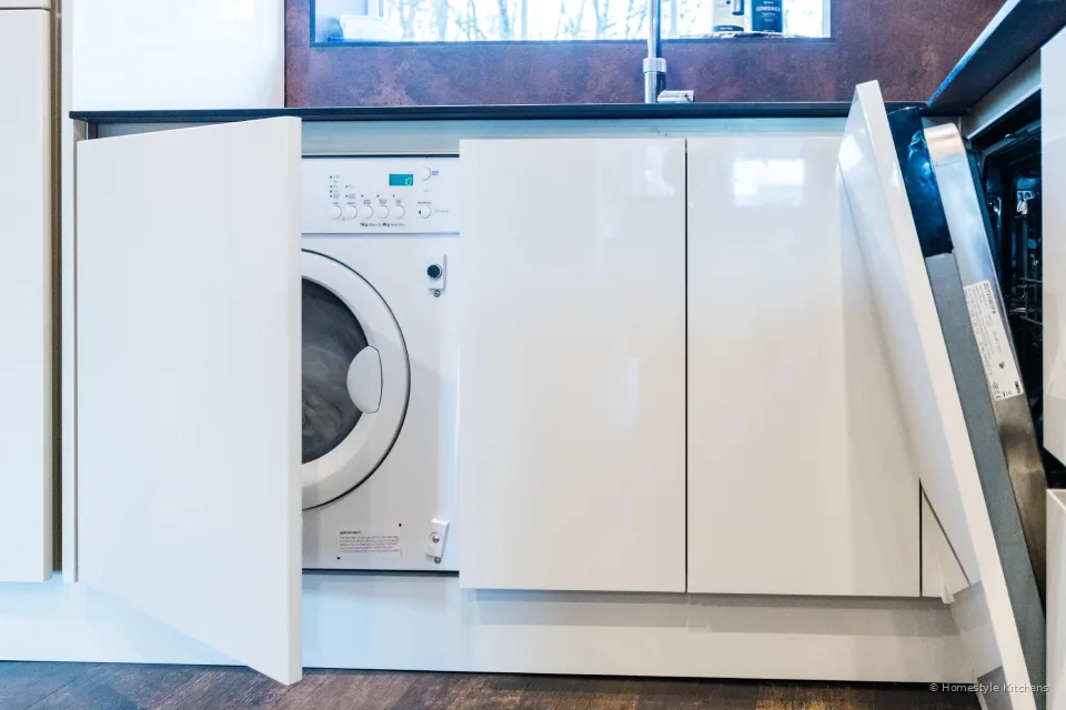 Integrated washing machine and dishwasher behind open gloss white handleless doors.