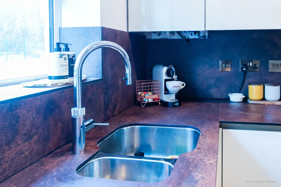 Sink corner with chrome tap, coffee machine and copper-effect splashback, gloss white wall cabinets.