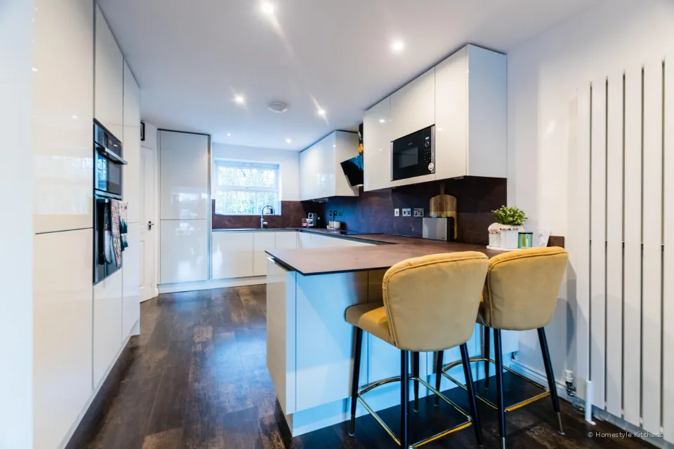 Gloss white tall units and oven housing, looking through to a peninsula breakfast bar and copper-effect worktop.