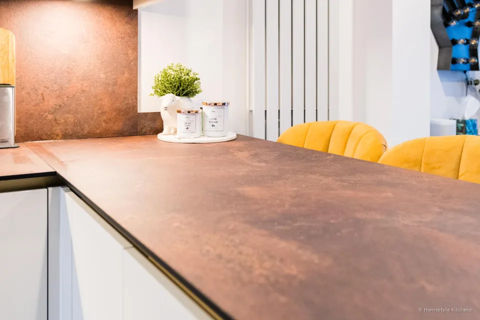 Copper-effect peninsula worktop looking toward mustard breakfast-bar stools.
