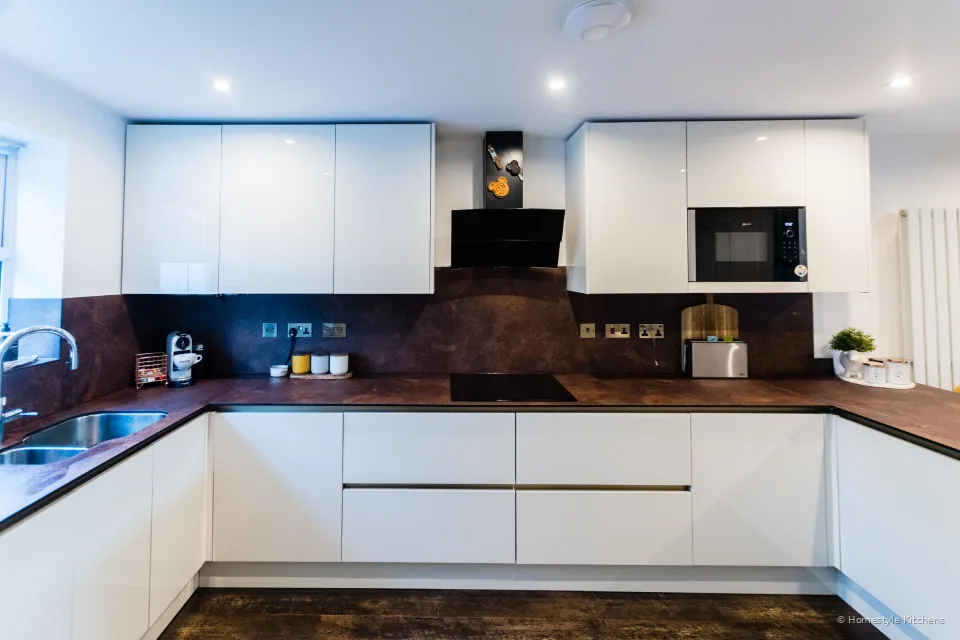 Gloss white handleless kitchen, copper-effect worktop and splashback, black hob and angled extractor.