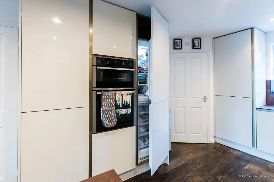 Gloss white tall housing with a black double oven and an open integrated fridge.