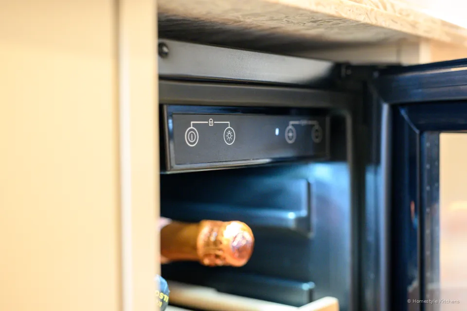 Inside a black wine cooler, bottle on a wooden rack and a digital display.