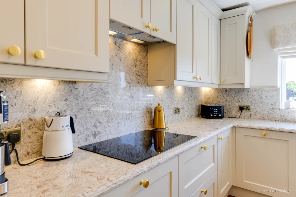 Black induction hob in marbled quartz, cream wall cabinets and extractor lights above.