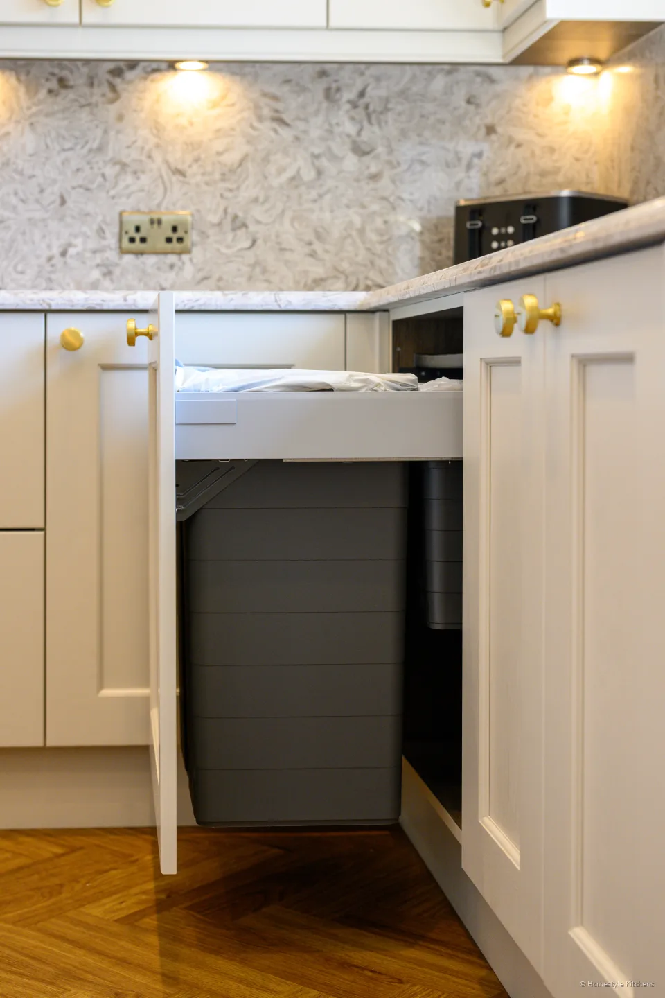 Integrated bin pull-out open in a cream cabinet, herringbone floor.
