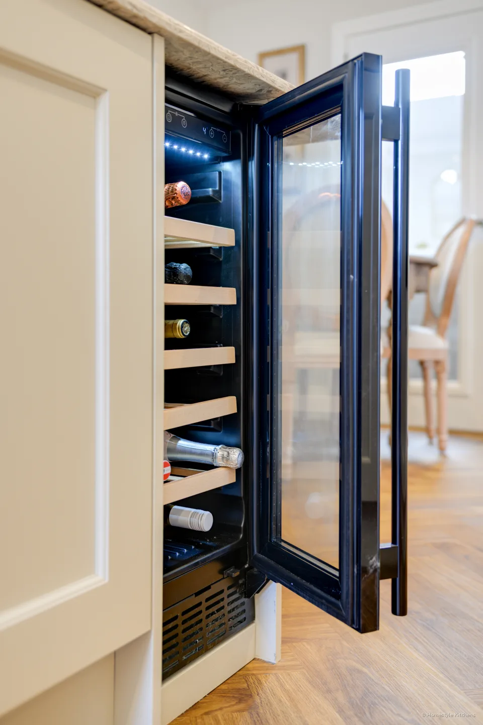 Black wine cooler open in a cream island, bottles on wooden racks.
