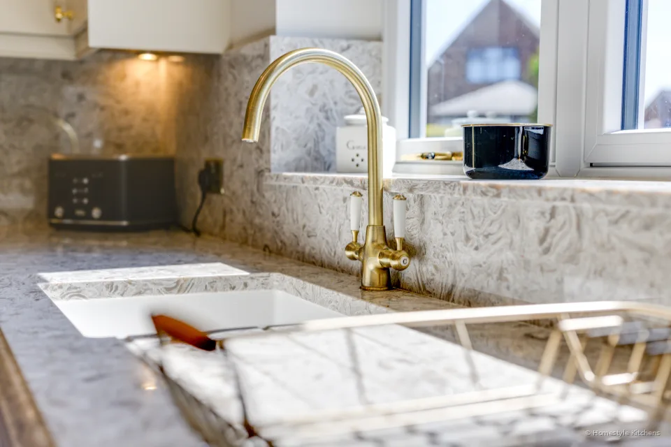 Brass twin-lever tap over a white Caple undermount sink, quartz worktop and window.