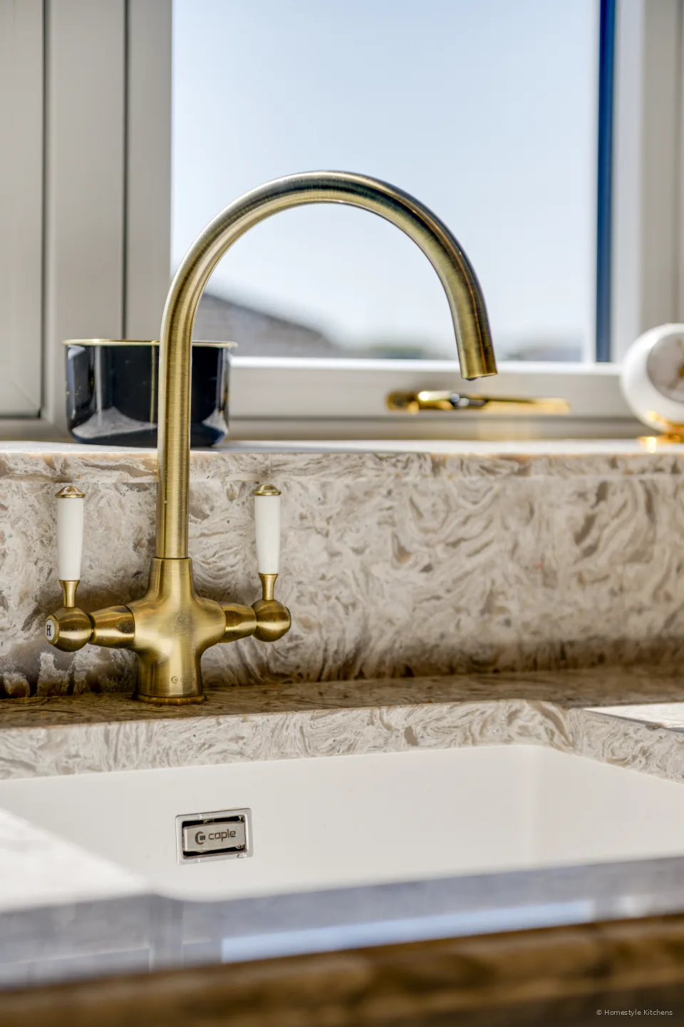 Brass twin-lever tap over a white Caple undermount sink in marbled quartz.