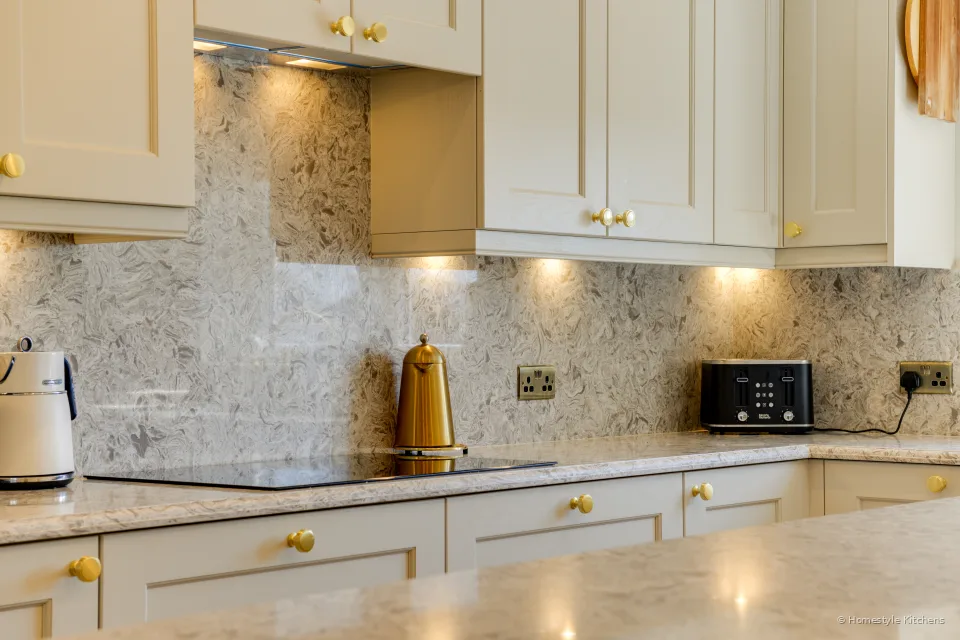 Black induction hob in marbled quartz, brass sockets and cream wall cabinets above.