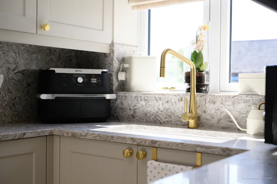 Brass tap and white sink under a window, black countertop oven on the quartz.
