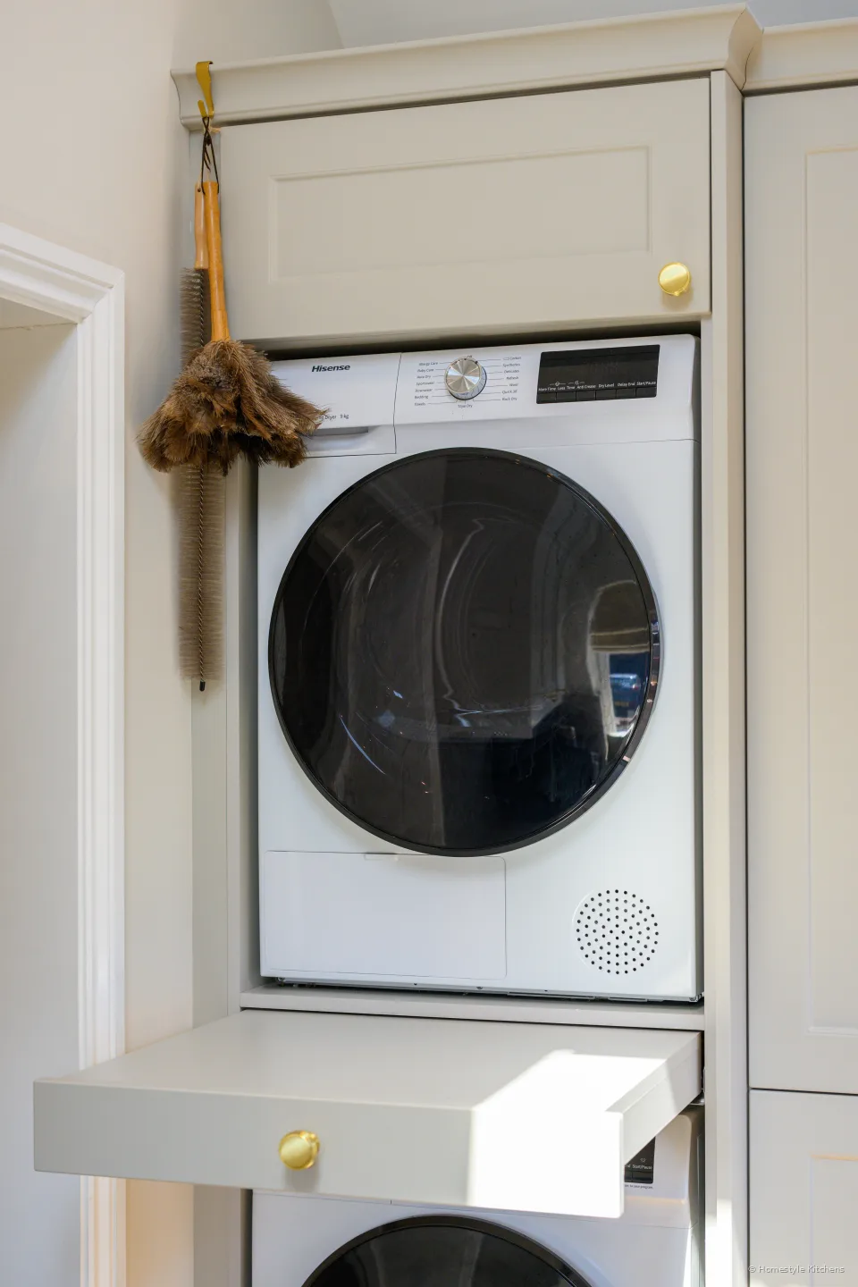 Stacked washer and dryer in cream painted housing, pull-out shelf extended between them.