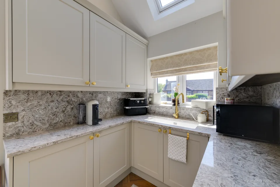 Cream painted utility run to the window, marbled quartz worktop, brass tap and a microwave on the right.