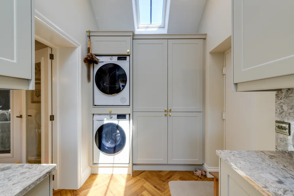 Cream painted utility with stacked washer and dryer in a tall housing, herringbone floor and a rooflight.