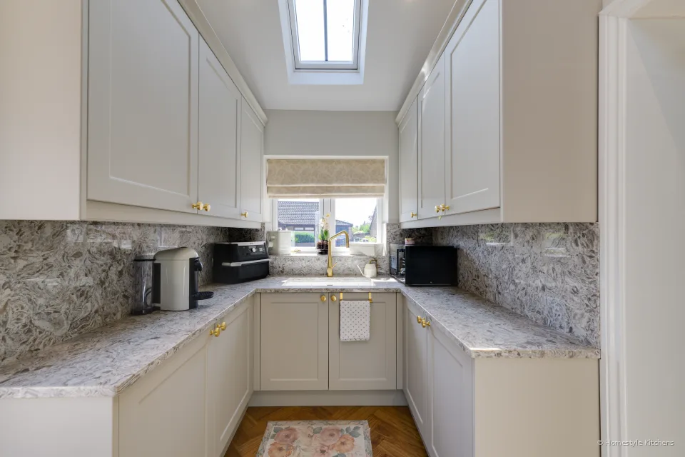 U-shaped cream utility with marbled quartz worktops and splashback, window over the sink and a rooflight above.