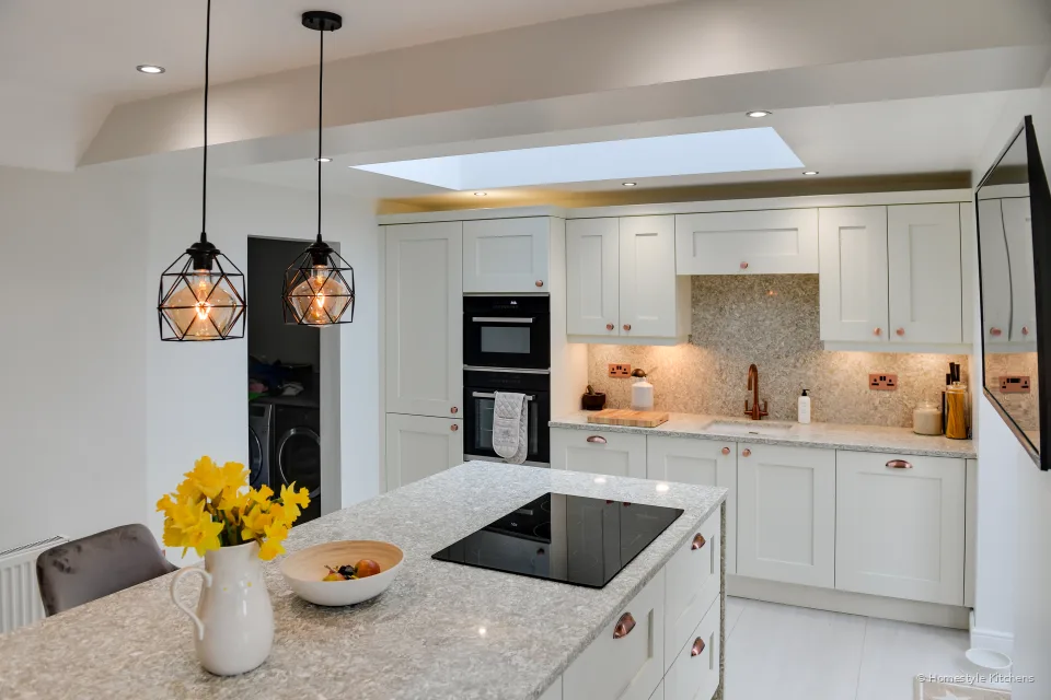 Ivory shaker kitchen island with a black induction hob, copper cup handles and yellow daffodils, ovens on the back run.