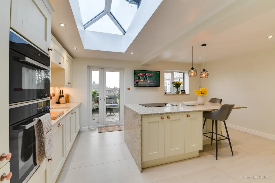 Ivory shaker kitchen with a quartz island, two grey stools, roof lantern and a TV on the wall.