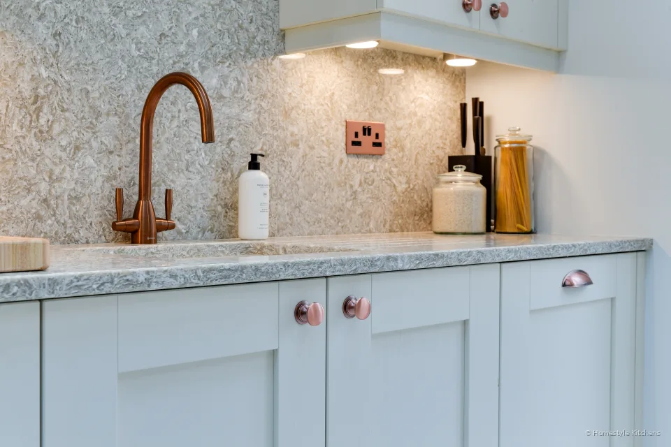 Copper swan-neck tap over an undermount sink in Chicstone Crema quartz, copper socket on the splashback.