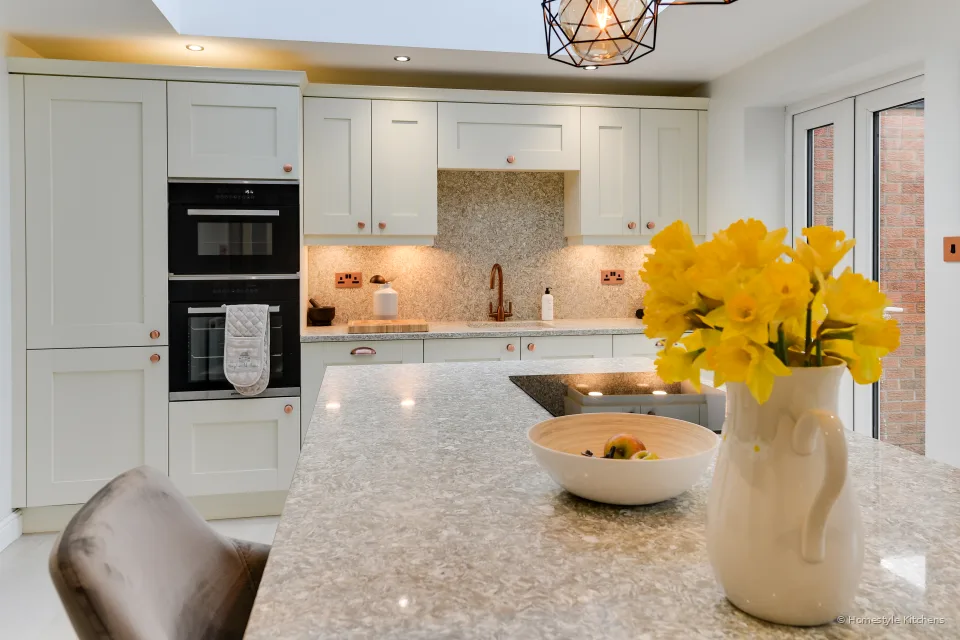 Yellow daffodils and a bowl on a Chicstone Crema quartz island, ivory shaker cabinets behind.