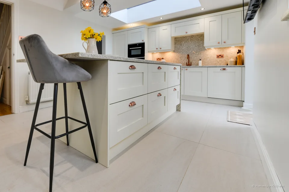 Grey bar stool at an ivory shaker island, looking down the kitchen under a roof lantern.