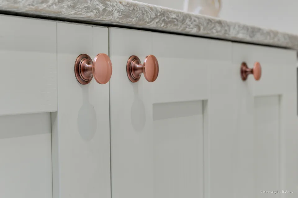Close-up of copper knobs on Fenwick Legno Ivory shaker doors under a quartz worktop.