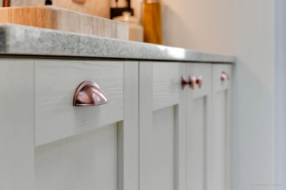 Close-up of a copper cup handle on an ivory shaker drawer under Chicstone Crema quartz.