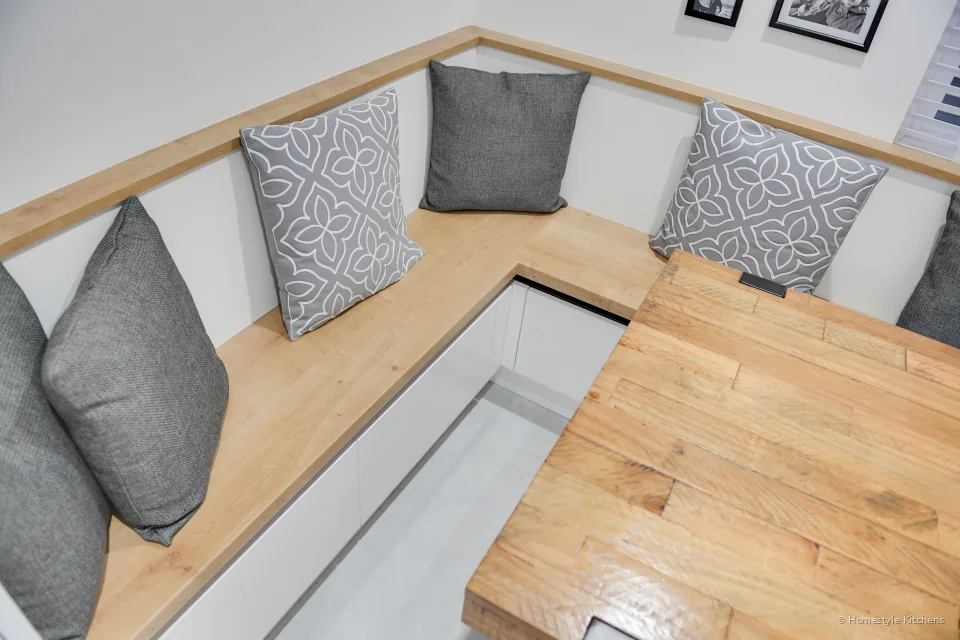Looking down on a built-in oak banquette with grey and patterned cushions and the corner of an oak table.