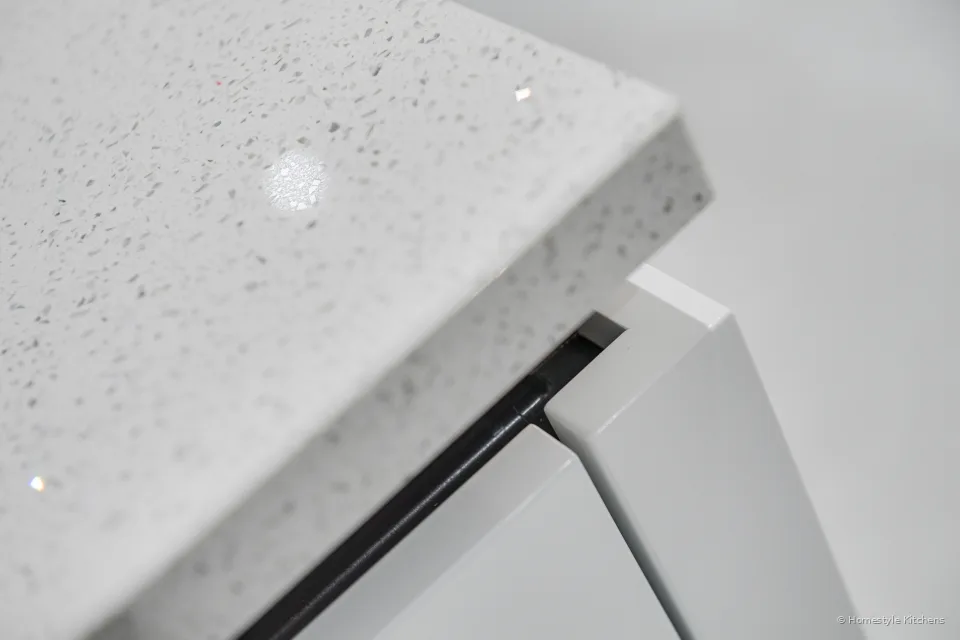 Close-up of white sparkle quartz meeting a white gloss handleless door and black rail.