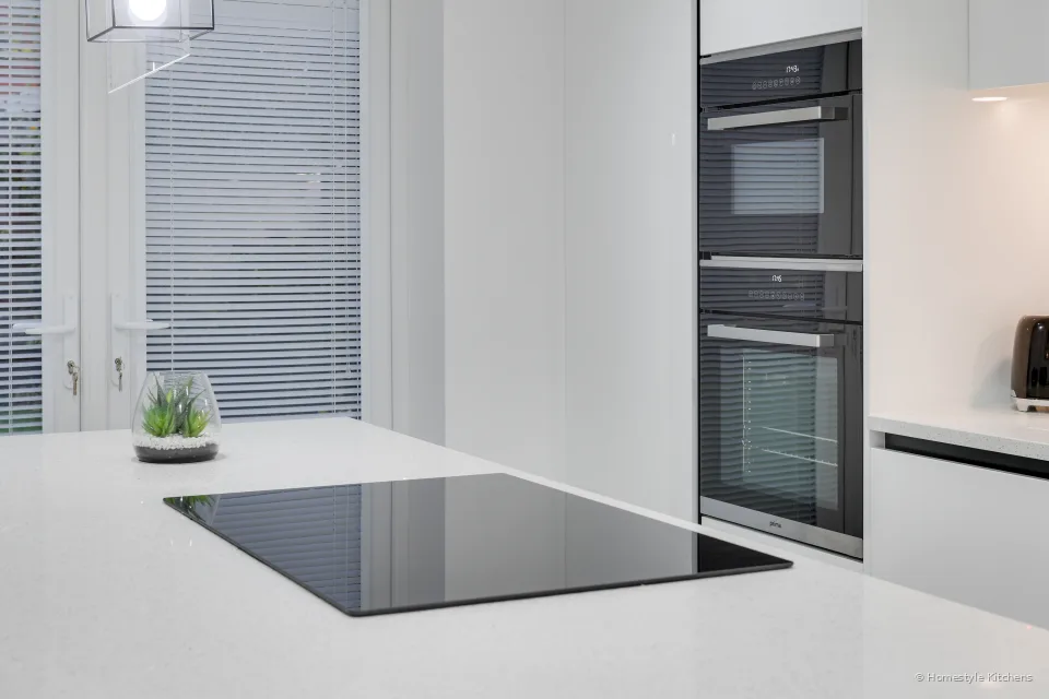 Black induction hob in a white quartz island, oven and combi microwave in the tall unit to the right.