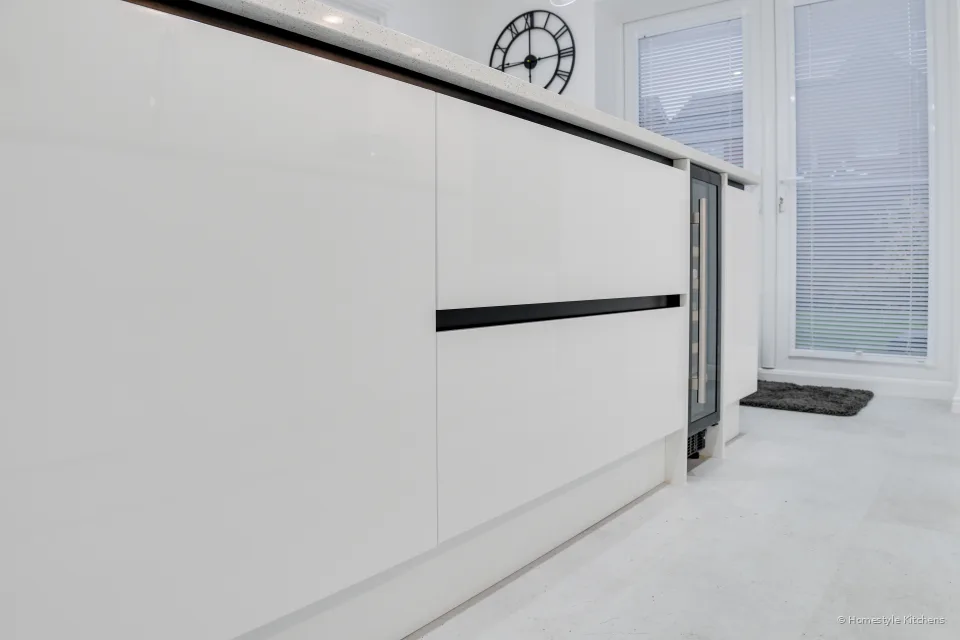 White gloss handleless island drawers with a black rail and a built-in wine cooler at the end.