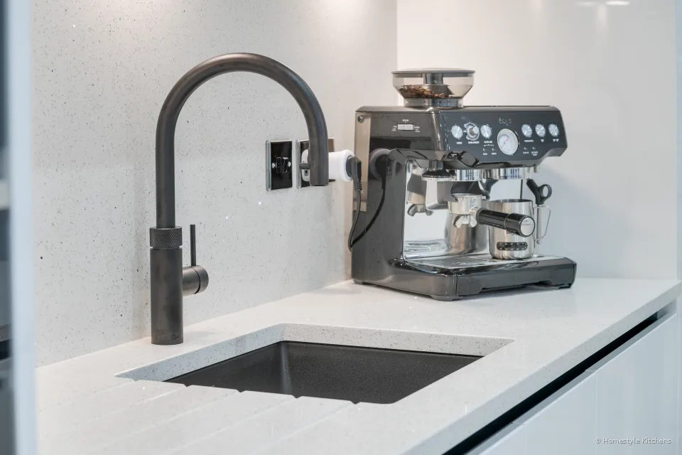 Black tap and black undermount sink in white sparkle quartz, coffee machine to the right, matching quartz splashback.