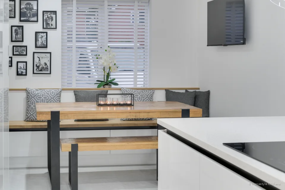 Dining nook from the kitchen island, oak table and built-in bench, white quartz island edge with a hob in the foreground.