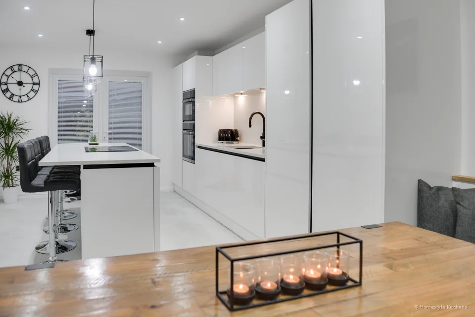 Oak dining table with a black candle holder, looking through to a white gloss island and the main run of kitchen units.