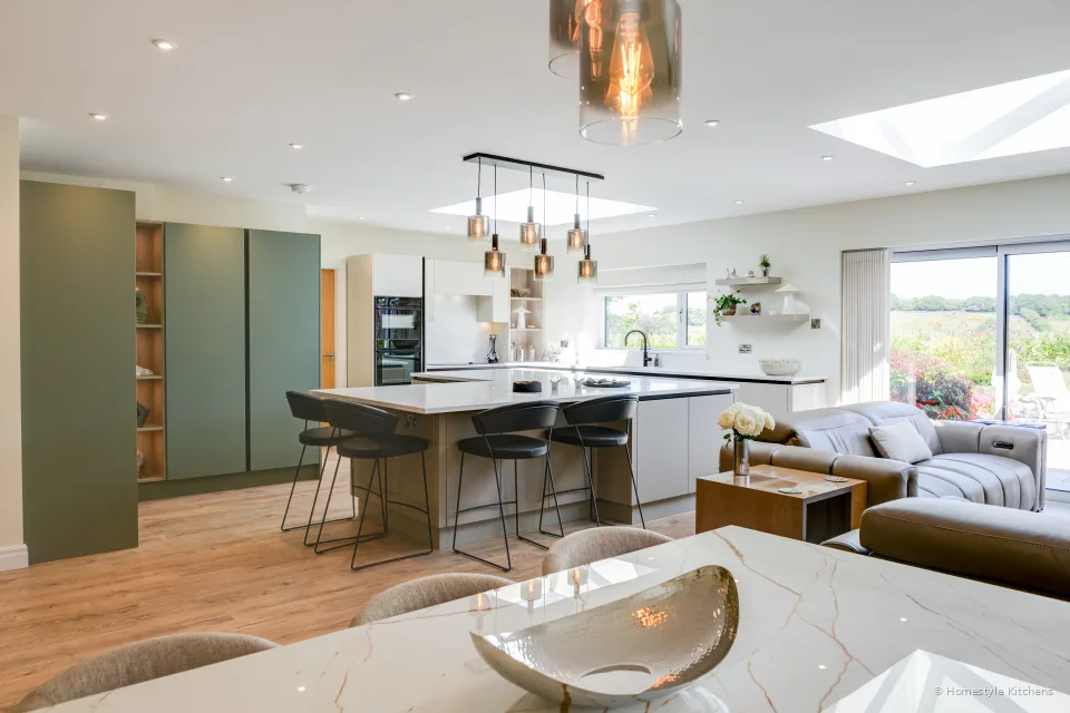 Kitchen from the dining end: island, reed green talls and the sitting area beyond.