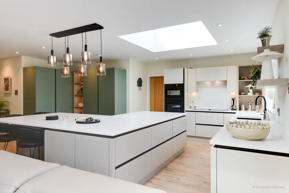 Island end-on under skylights, black hob in white quartz, copper pendants.