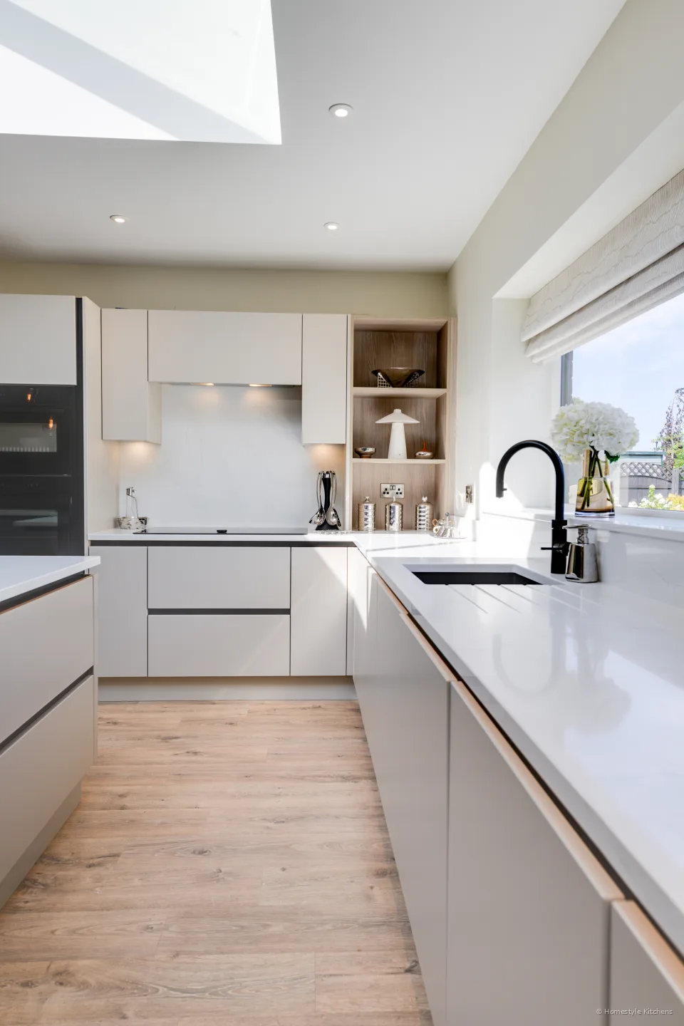 Sink and black tap under a window, cream base units, quartz upstand.