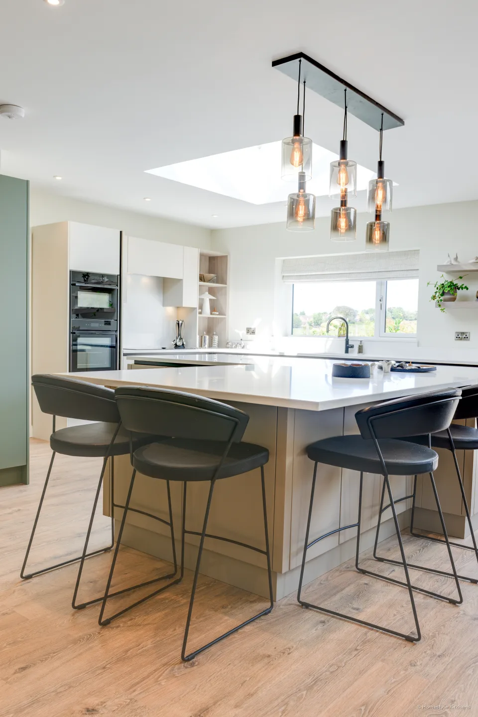 Dining table and stools under a linear pendant, kitchen beyond.